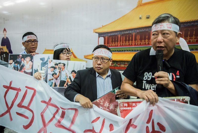 2017年1月9日，支聯會時任主席何俊仁（右2）與李卓人（右1）、鄒幸彤（右3），在香港政府設置的北京故宮大型宣傳看板前，舉著六四事件中、絕食學生的著名標語「媽媽我餓，但我吃不下！」抗議港府當時強推的香港故宮文化博物館計畫。「當我們看到故宮時，我們記得的，不是裡面的文物，」曾親身經歷六四事件的李卓人表示，「我們記得是外面的坦克車，我們聽到的是外面的槍聲。」（攝影／ISAAC LAWRENCE / AFP）