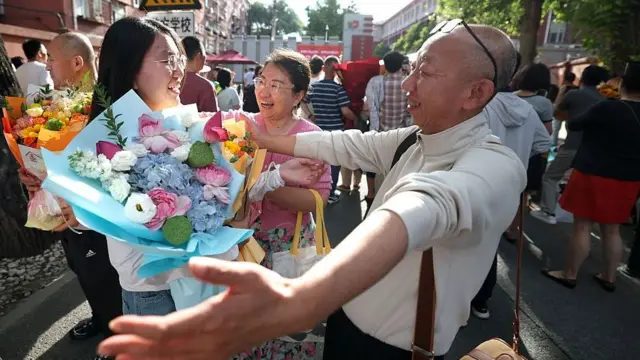 2026年6月10日，在中国北京，一名女学生在2026年全国高考结束后，在考场外被父亲拥抱。她笑容灿烂，手里拿着一束花。