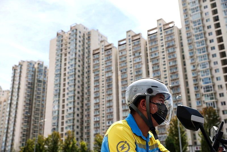 一名外送員騎著電動車經過高樓大廈。2026年7月，中國70個大中城市新建商品住宅價格較去年同期下降3.2%。 （歐新社）