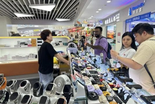 深圳周期上午设计次日量产 从华强北到人形机器人 1 店員為外國顧客介紹有AI功能的商品。(深圳晚報)