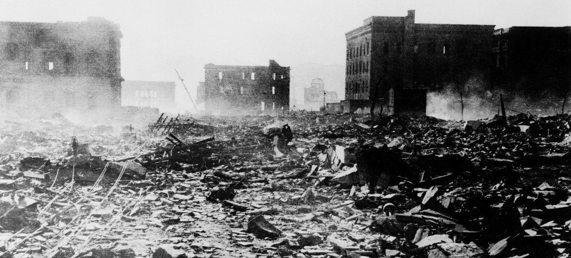 一张黑白照片展示了 1945 年日本广岛原子弹爆炸后的废墟与破坏景象，背景中的原子弹圆顶在断壁残垣中清晰可见。
