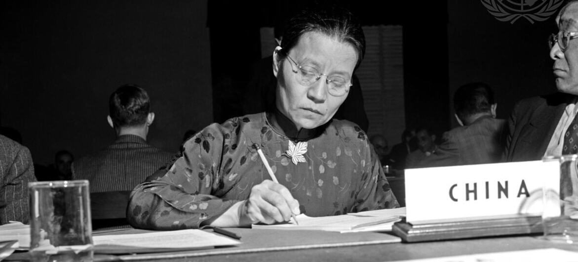 【专题报道】从谈判桌到维和一线:四位女性,如何改变联合国 1 吴一芳在一张大会议桌旁写笔记,桌子旁边放着一块中国标牌,背景中可以看到United Nations徽标。