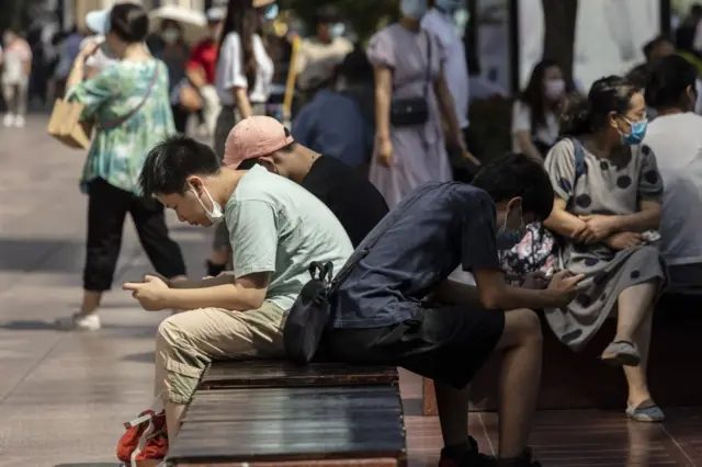 一些人坐在横凳上，在看手机