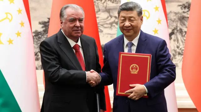 北京人民大会堂内塔吉克总统埃莫马利·拉赫蒙（左）与中国国家主席习近平（右）握手，习近平左手抱着两国刚签署交换的协议文本（12/5/2026）