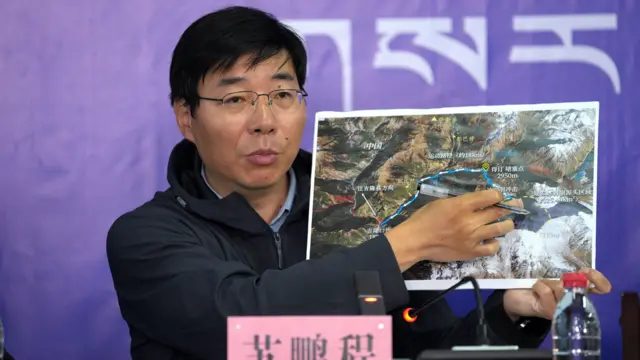西藏吉隆镇新闻发布会现场，中国科学院成都山地所研究员苏鹏程举起一张卫星照片讲解中方认定的事发经过（中新社图片30/8/2026）