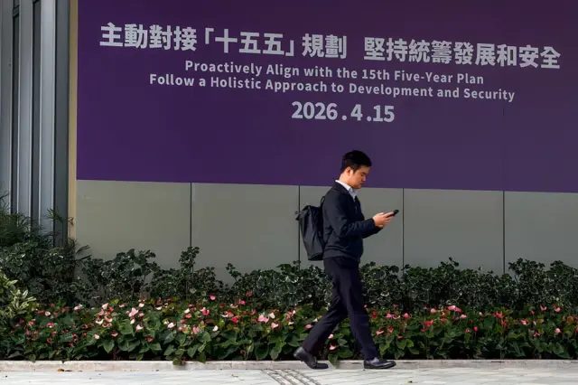 2026年3月17日：一名男子走过香港政府总部外的一幅大型紫色政府横幅。该横幅宣传积极对接国家“十五五”计画（2026-2030年），强调统筹发展与安全。