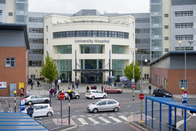 考文垂大学医院（University Hospital）外观。医院设有半圆形入口，配有窗户及宽阔大门，两侧为红砖建筑。门外停泊着多辆汽车。
