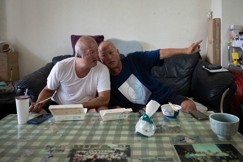 沙利窦迈药害60年 台湾3位「沙儿」的生命故事 7 沈宗義(右)靠近重聽的沈宗德(左),為他解釋世界。這時電視上播著求職訊息,找到工作正是沈宗德的期盼。(攝影/謝佩穎)