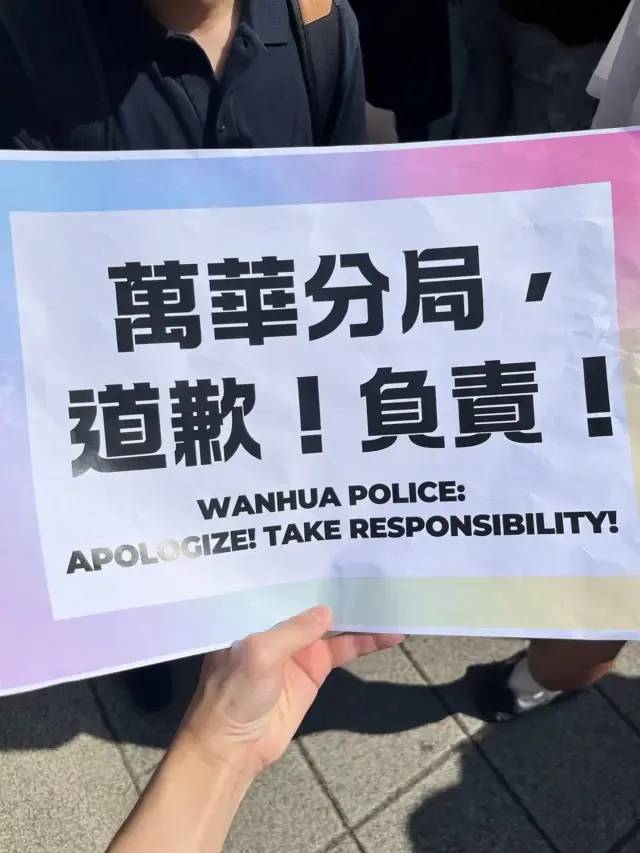 台北西门町 LGBT 社群抗议现场，一位示威者手持“万华分局，道歉！负责！”中英文标语牌（4/10/2026）