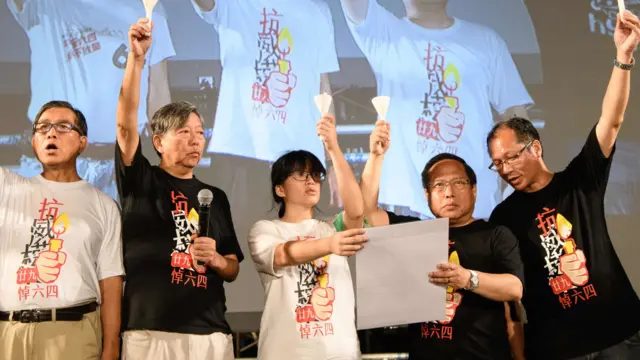 李卓人（左二）、邹幸彤（中）、何俊仁（右二）在香港维多利亚公园“六四”烛光晚会主礼台上宣读祭词，各人伸出一只手高举白色蜡烛（4/6/2018）