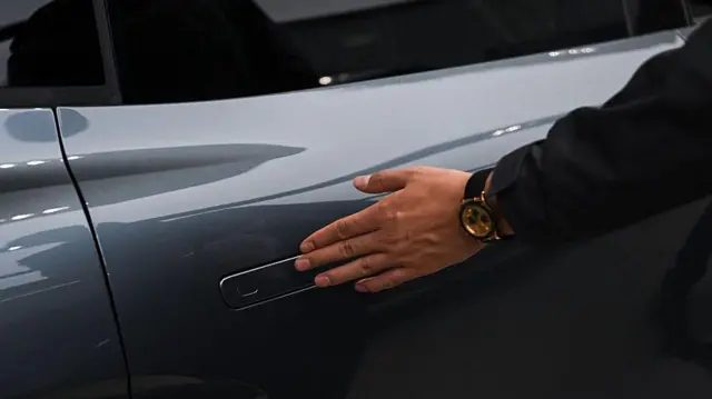 在中国的一次汽车路演中，一名男子正在检查一辆电动车，他的手轻轻拂过电动车的伸缩门把手。
