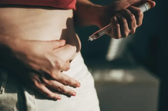 一名身材苗条的女子将一支减肥针拿在身前。