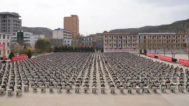 2015年4月11日，中国陕西省延安市宜川中学逾1,700名学生在学校操场上参加户外考试。大批学生坐在排列整齐的课桌前应试，桌椅分布于宽阔的操场上。学生之间保持一定距离，场面规模庞大。背景可见操场设施、校园建筑及周围环境，展现大规模集体考试的场景。