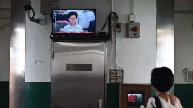 一名妇人在看电视，电视画面中是林郑月娥。