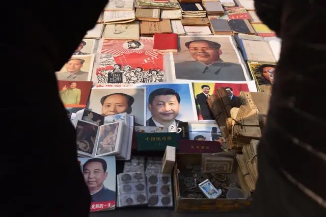 地摊上摆着毛泽东、习近平、华国锋的画像、画册，以及其他商品。