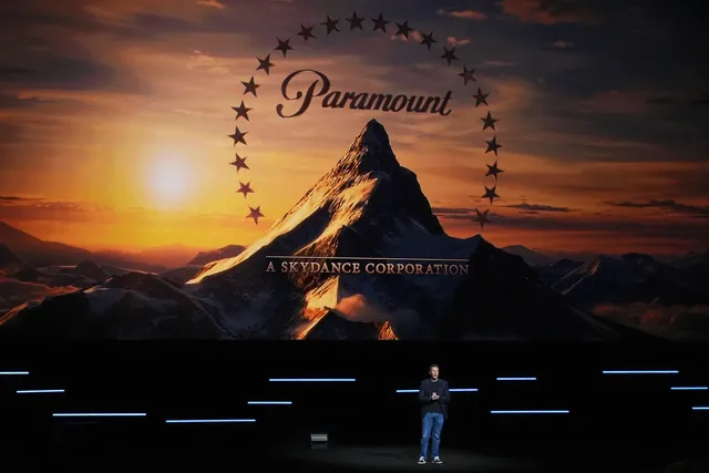 一个人站在舞台上，身后的大屏幕上是派拉蒙（Paramount）的雪山标志和“A SKYDANCE CORPORATION”字样