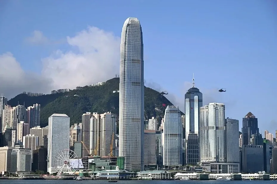 海边一片高楼，中间是一座很高的玻璃幕墙大厦，后面是山，左下有一座摩天轮