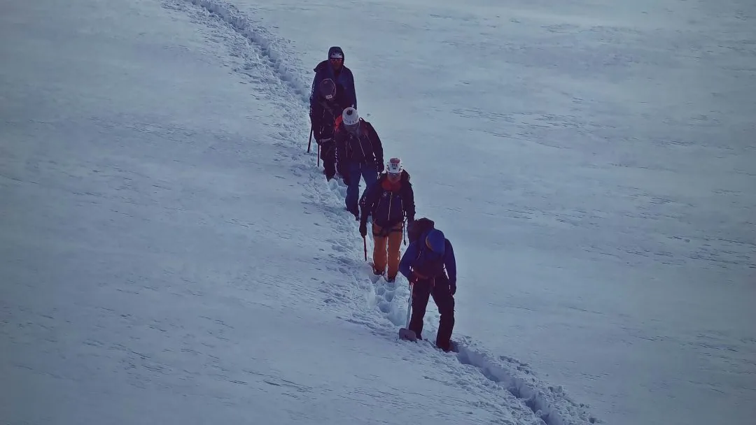 四名登山者沿雪坡上的脚印行进（资料照片）。