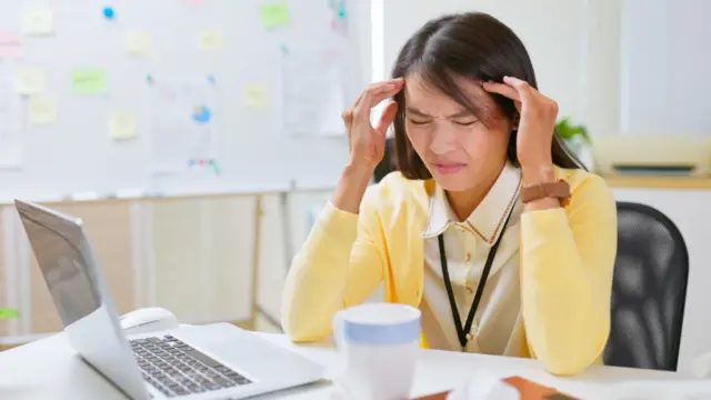 设计图片：在台湾，一位女士坐在办公桌前，表情看似头疼不堪，状甚痛苦