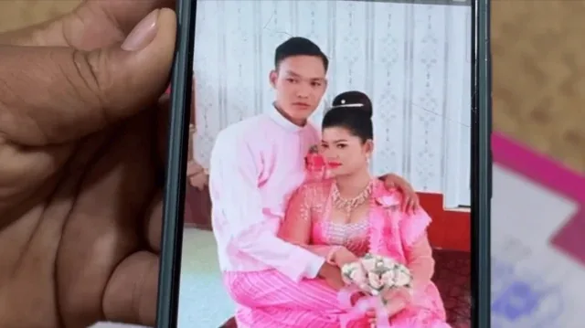 一只手拿着手机。手机萤幕上可见一名男子和一名女子身穿粉红色与白色礼服相拥而立，女子手持一束白色鲜花。