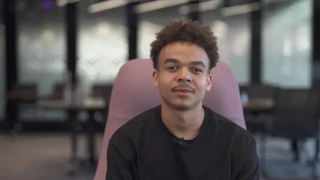 英国口音焦虑调查:每10人中1人因口音在职场感到不安 2 一名年轻男子直视镜头;背景可见桌椅。