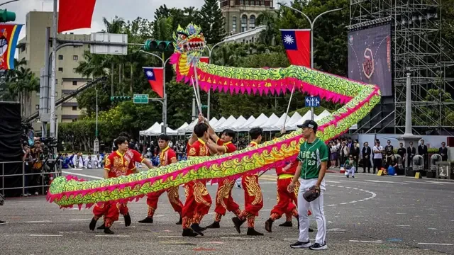 2026年10月10日台北国庆大会及庆祝活动期间，一支传统舞龙队伍舞动绿色巨龙，身旁有一名棒球选手同行。