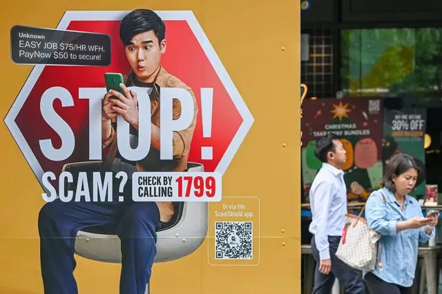 这张拍摄于2025年12月9日的照片显示，人们在新加坡莱佛士坊（Raffles Place）金融商业区走过一张警告诈骗威胁的海报。随着授权此项惩罚的法律生效，自12月30日起，新加坡的诈骗犯若涉严重案情，将面临强制性最高 24 鞭的鞭刑。