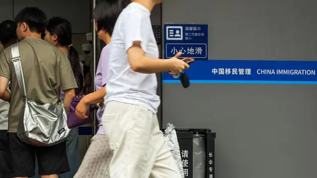 2026年8月1日，广东省深圳市，人们走进出入境管理服务大厅，一名行人从“中国移民管理”标志旁经过。 
