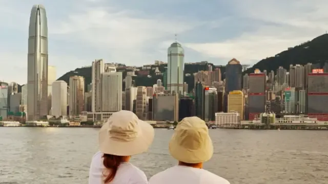 戴上渔夫帽的Eric和Emily背向镜头，望向维多利亚港与香港岛北岸风景