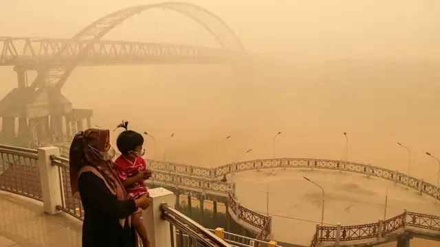 印尼中加里曼丹省帕朗卡拉亚地区，戴着口罩的母亲和孩子站在桥上眺望，森林和土地火灾产生的浓厚烟雾笼罩四周一切（12/10/2026）