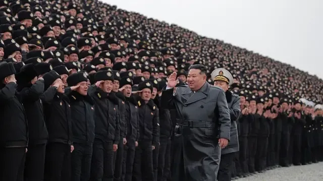 朝鲜领导人金正恩身穿深色长外套，走过列队敬礼的制服官兵，当时正值一场大型军事集会。